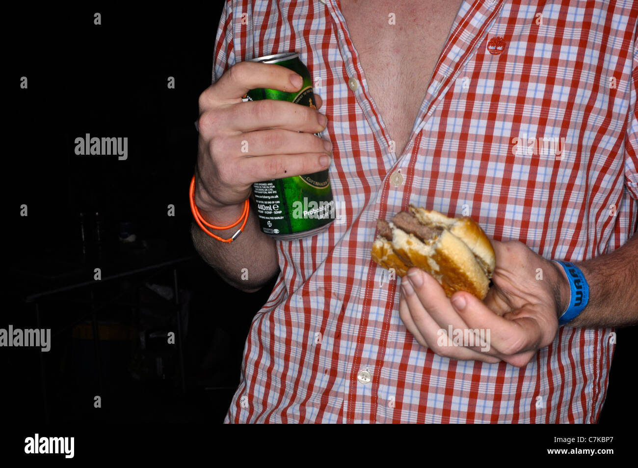 A party goer at a festival eating a burger and drinking a beer Stock Photo