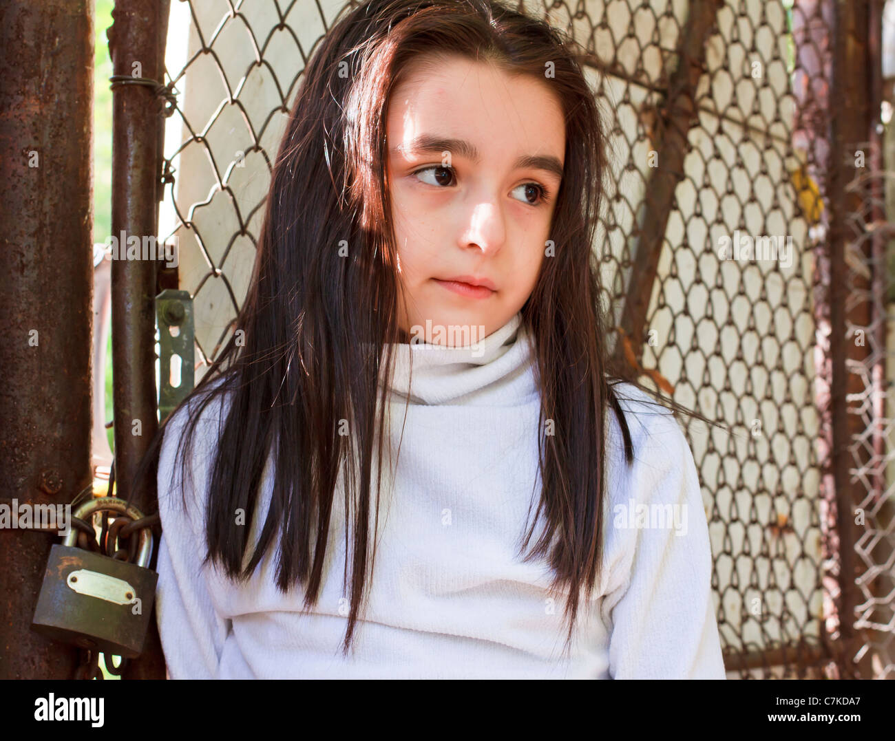 Sad and scared little girl in front of a wire fence Stock Photo
