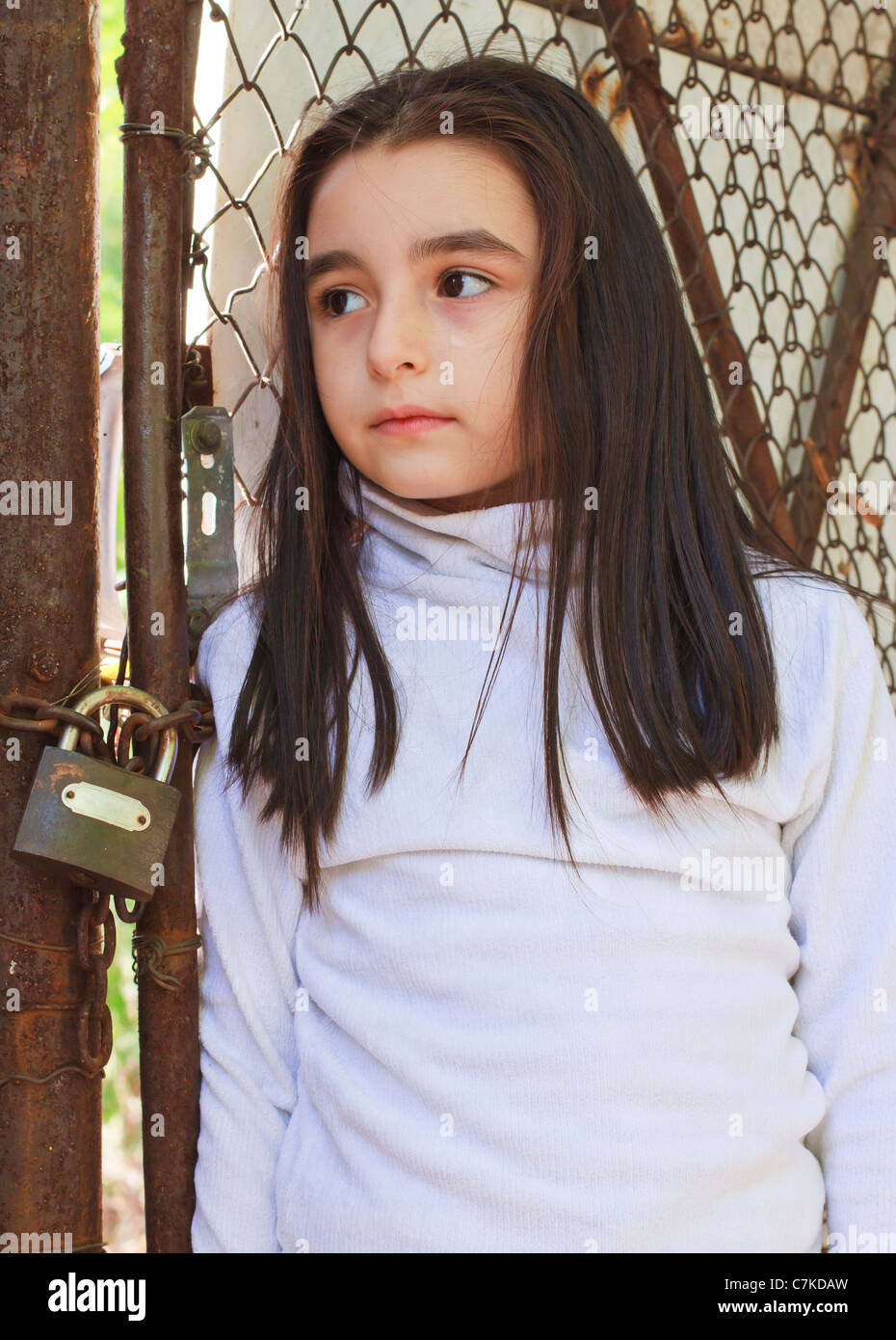 Sad and scared little girl in front of a wire fence Stock Photo