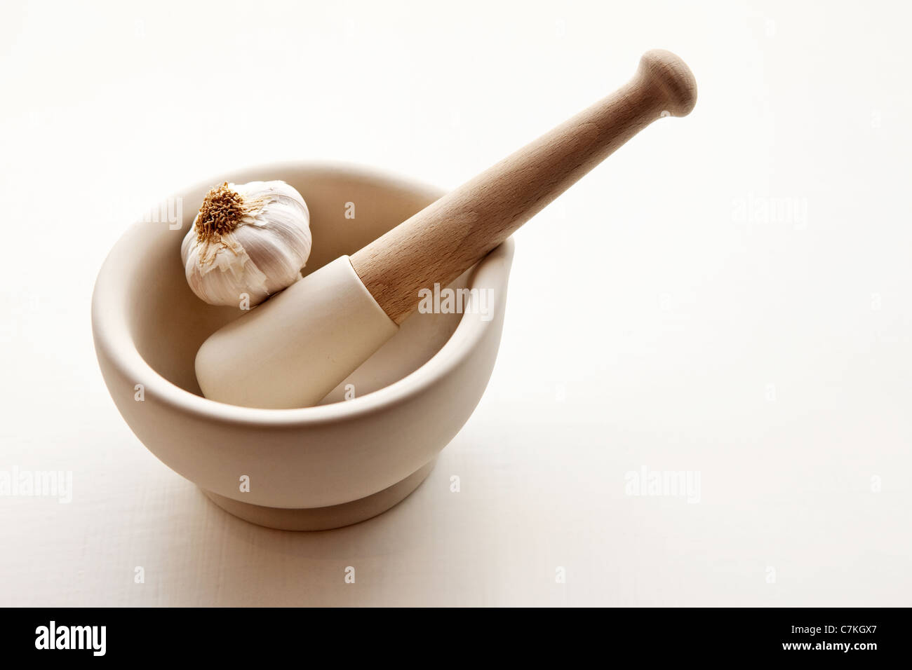 A mortar and pestle with a clove of garlic against a white background