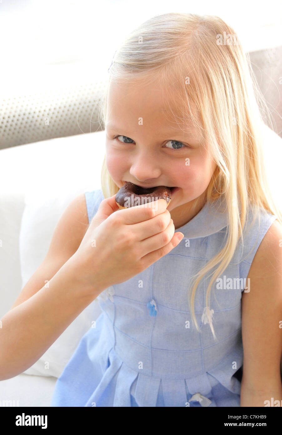 Young girl, 6, with a blue dress and a chocolate donut in her hand Stock Photo