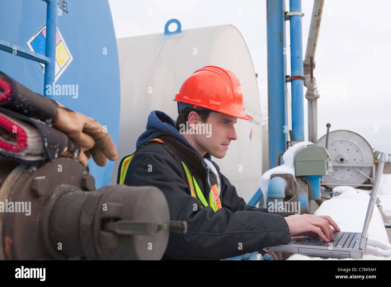 Engineer recording data on a laptop near a fuel tankers site Stock Photo
