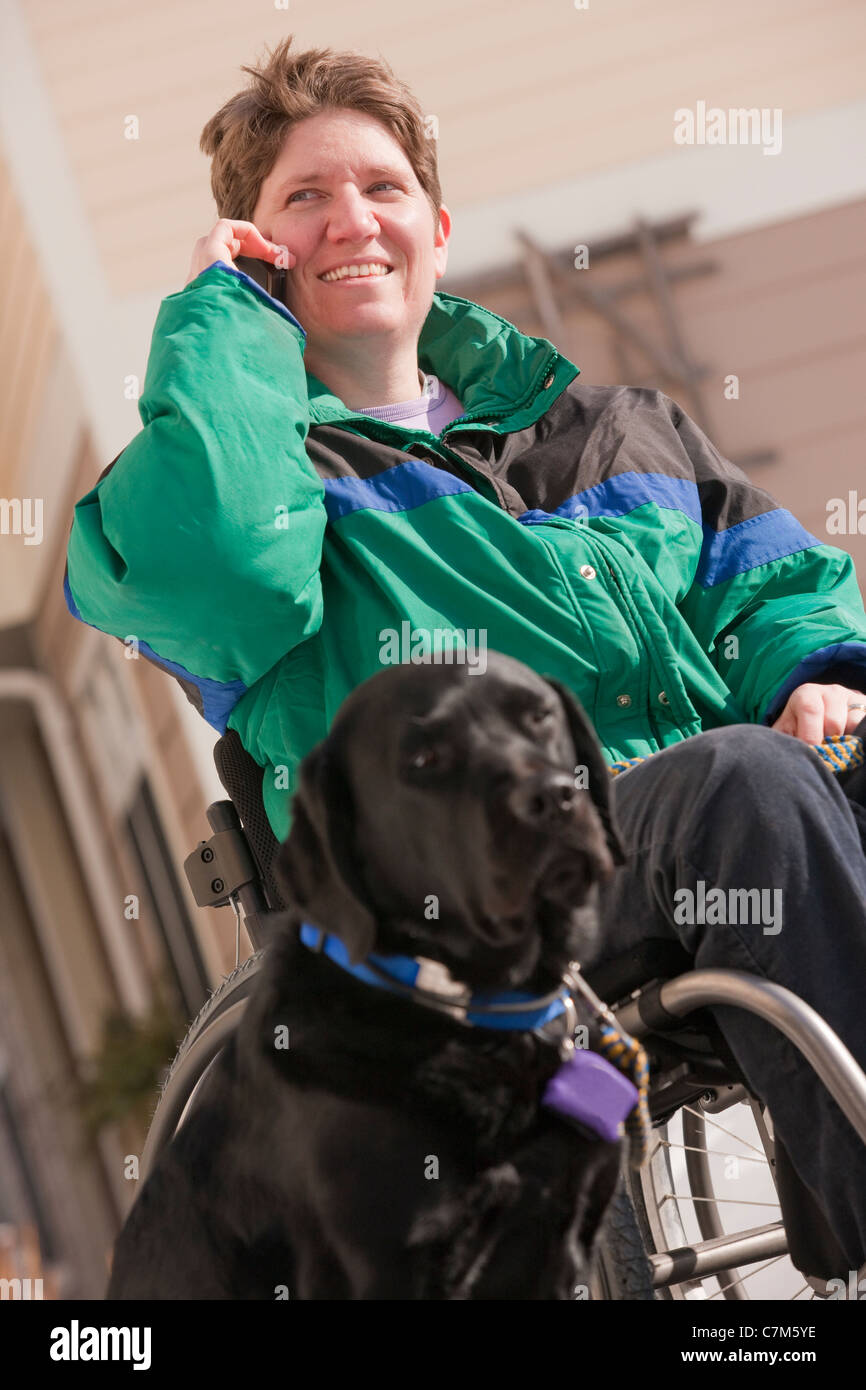 Woman with multiple sclerosis talking on a mobile phone with a service dog Stock Photo