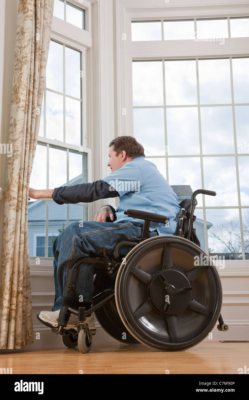 Man with spinal cord injury in a wheelchair looking out the window of his accessible home Stock Photo