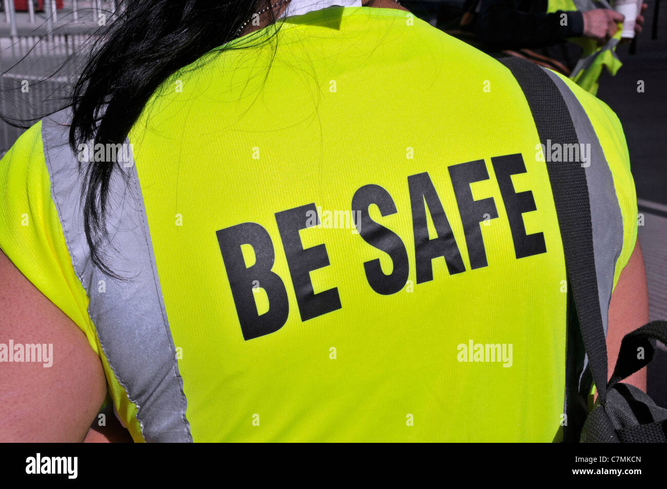 Close up back view of woman construction worker wearing a yellow high visibility vest jacket with Be Safe slogan London England UK Stock Photo