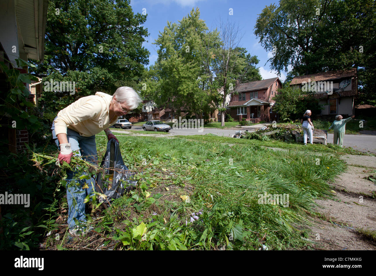Detroit, Michigan - Members of the Three Mile Drive block club clean trash and weeds from a vacant home in their neighborhood. Stock Photo
