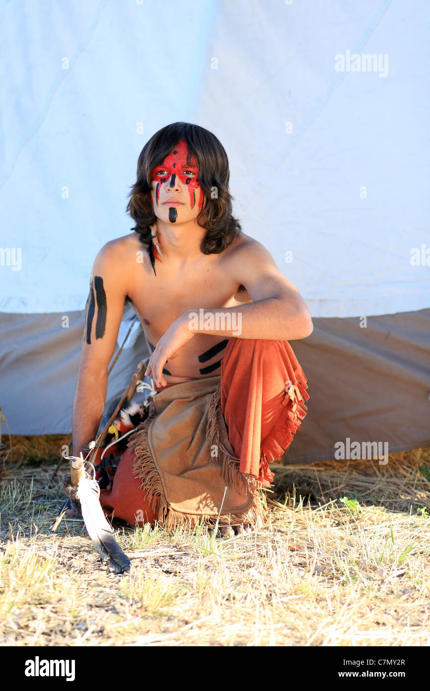 An American Indian Boy squats next to his tepee Stock Photo