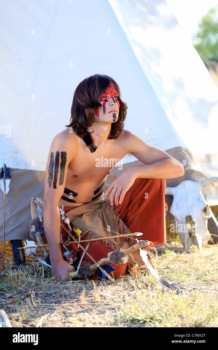 An American Indian Boy squats next to his tepee Stock Photo