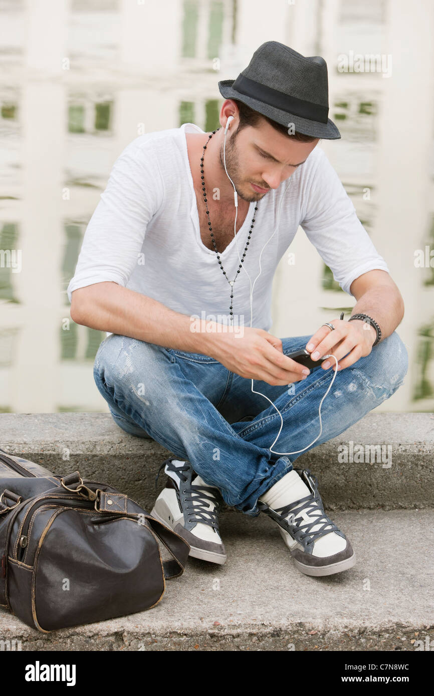 Man sitting on the ledge of a canal and listening to music with an MP3  player, Paris, Ile-de-France, France Stock Photo - Alamy