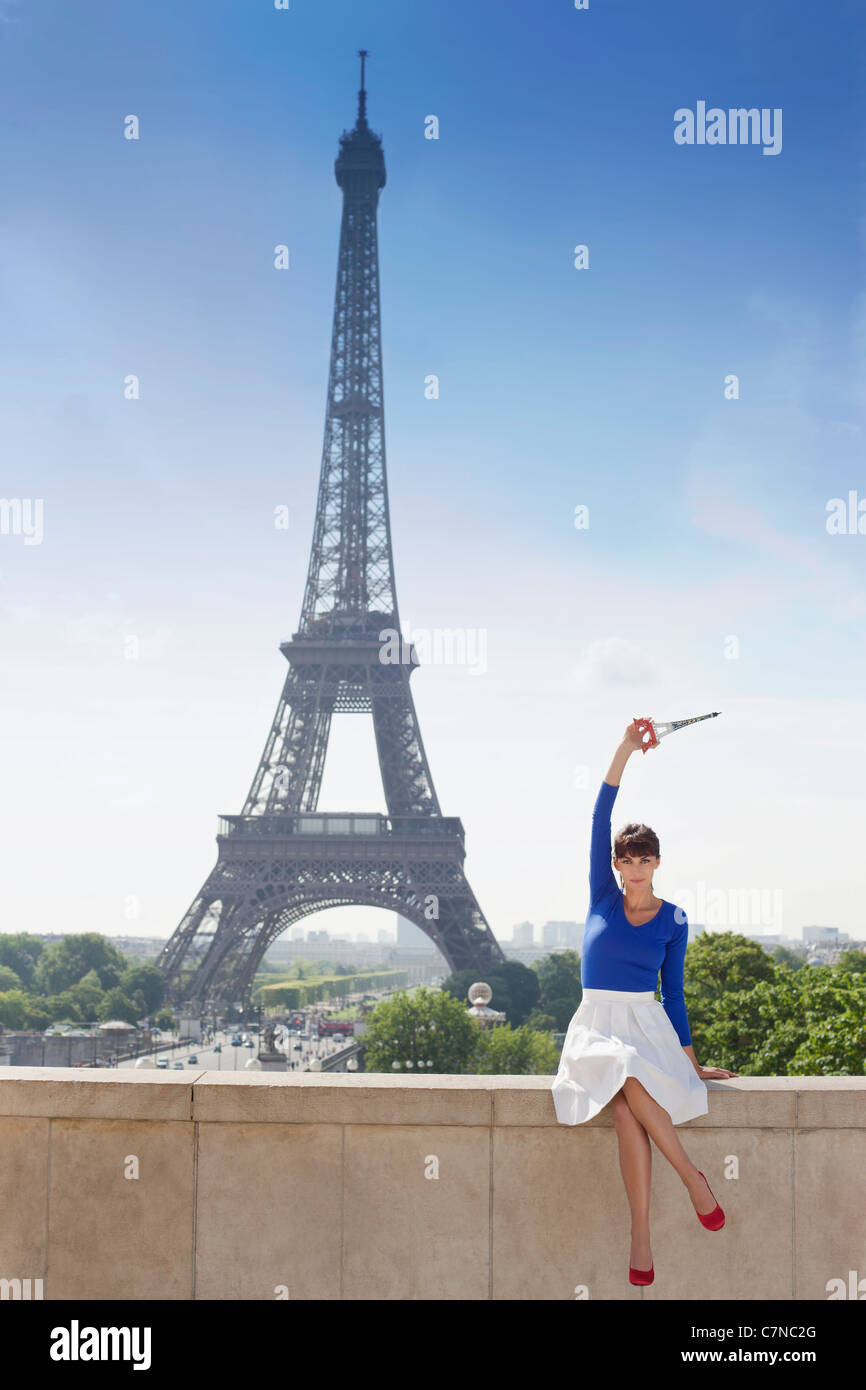 Woman holding replica of Eiffel Tower sitting on stone wall with Eiffel