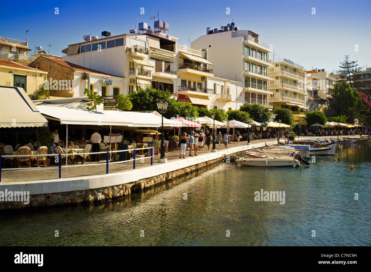 The waterfront on Lake Voulismeni in the centre of Agios Nikolaos on the Greek island of Crete bathed in late summer sunshine Stock Photo