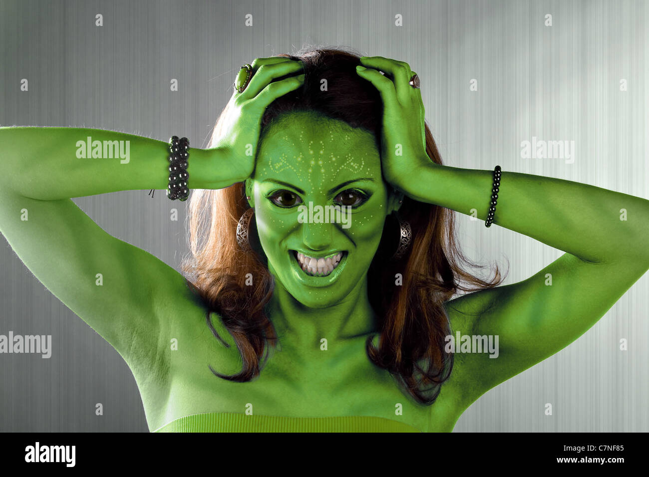 A green alien or Martian woman posing over a silver brushed metal backdrop. Stock Photo