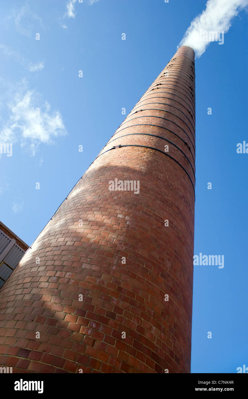 A tall brick factory smoke stack billowing with steam and smoke. Stock Photo