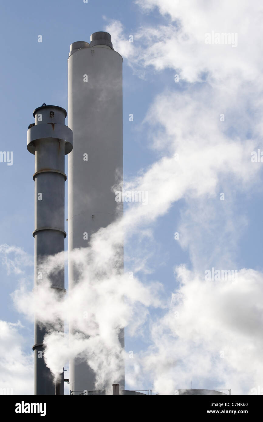 Steel smoke stacks atop buildings billowing with steam and smoke. Stock Photo