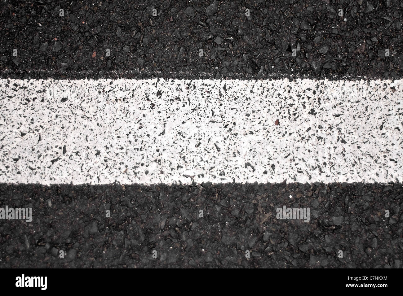 Closeup of a tar or asphalt pavement texture with a white line painted down the center. Stock Photo