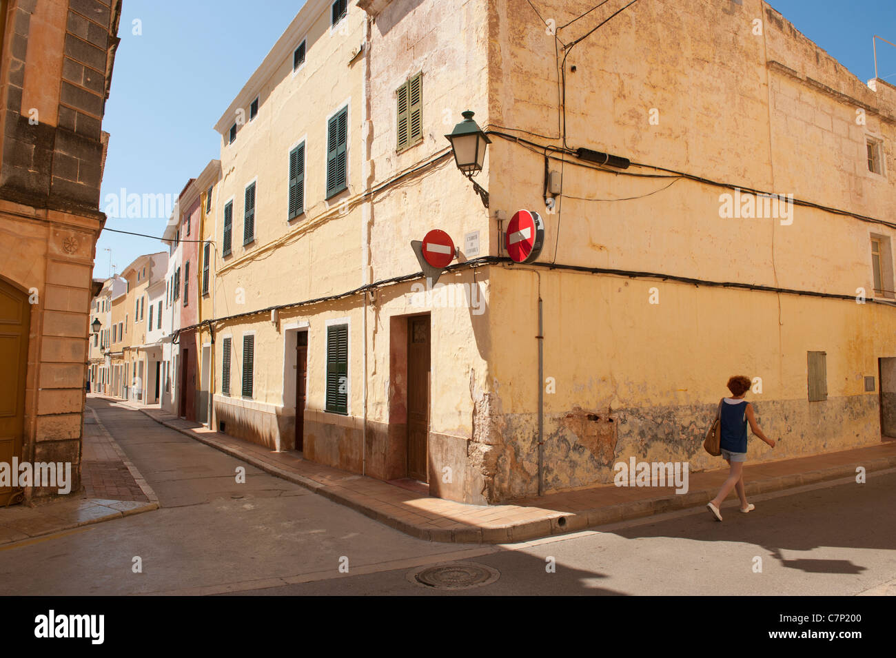 Alley in Minorca Spain, bright coloured building line a street with a woman walking. Stock Photo
