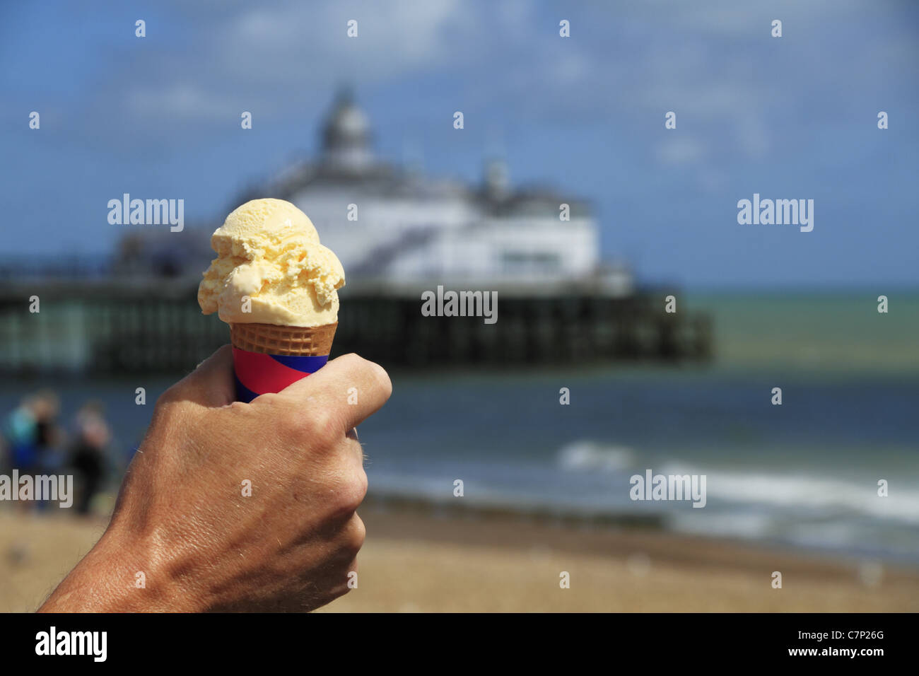 A man holds an ice cream on the beach with the Pier in the background