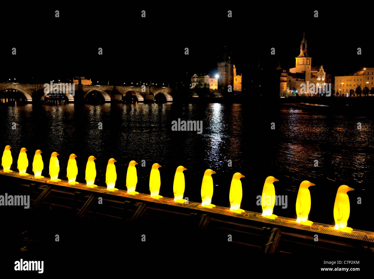Illuminated yellow penguins sculpture on the river in Prague Czech Republic with Charles bridge in the background Stock Photo