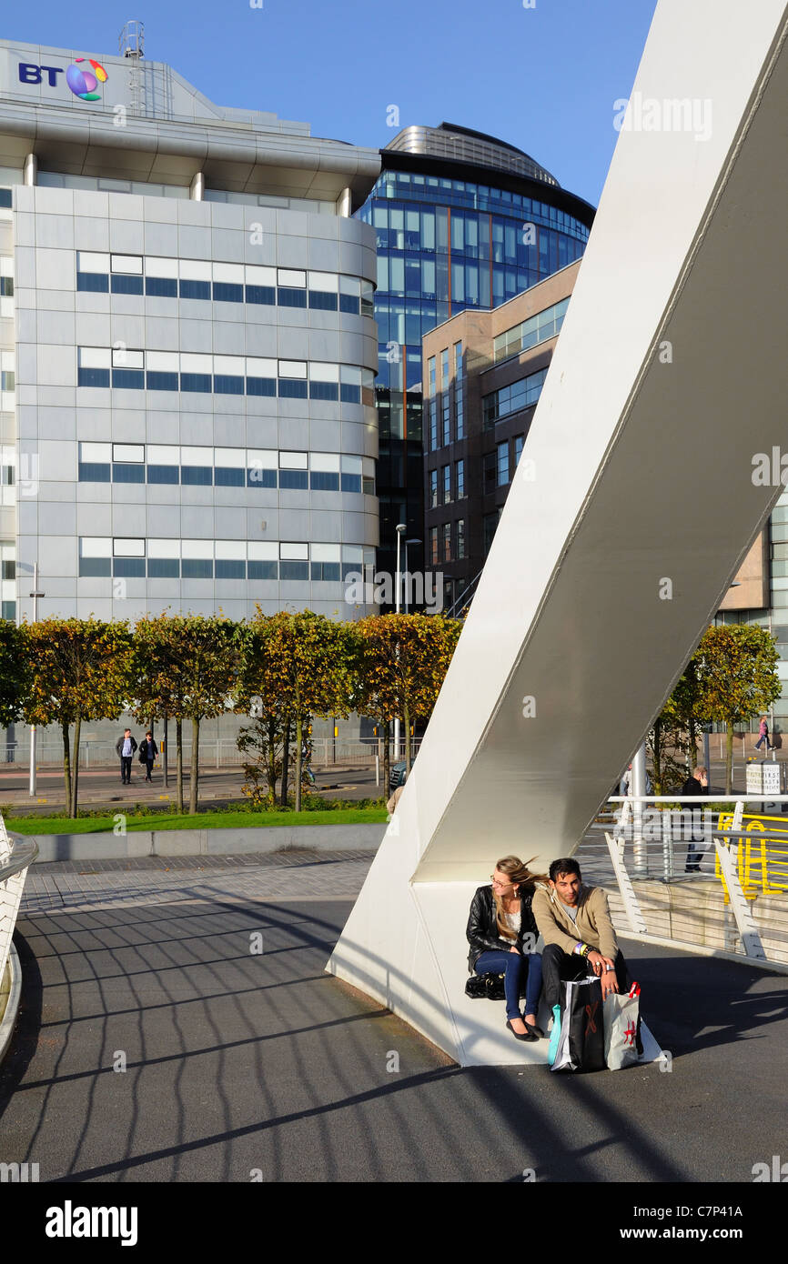 The Tradeston (Squiggly) bridge, two people sitting, British Telecom building in background in Glasgow, Scotland, UK Stock Photo