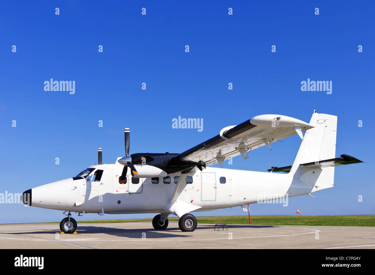 Photo of a twin propeller aircraft stationary on the runway on a bright sunny day with clear blue sky. Stock Photo
