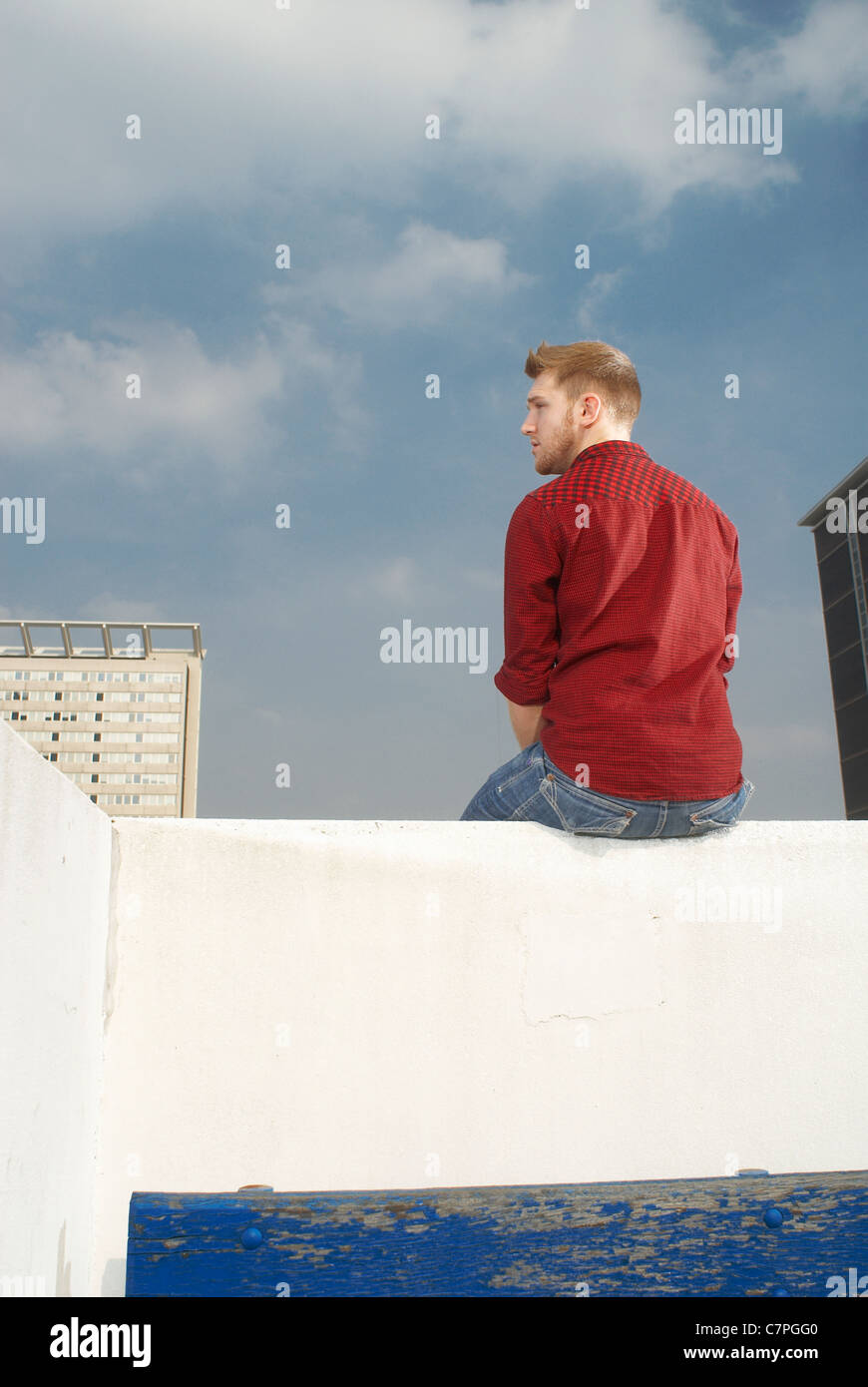 Man sitting on rooftop wall Stock Photo
