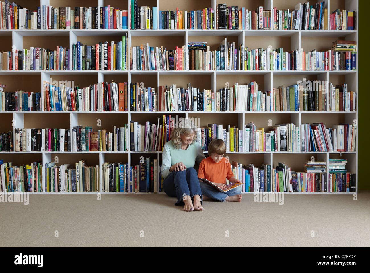 Woman reading with grandson by bookshelf Stock Photo