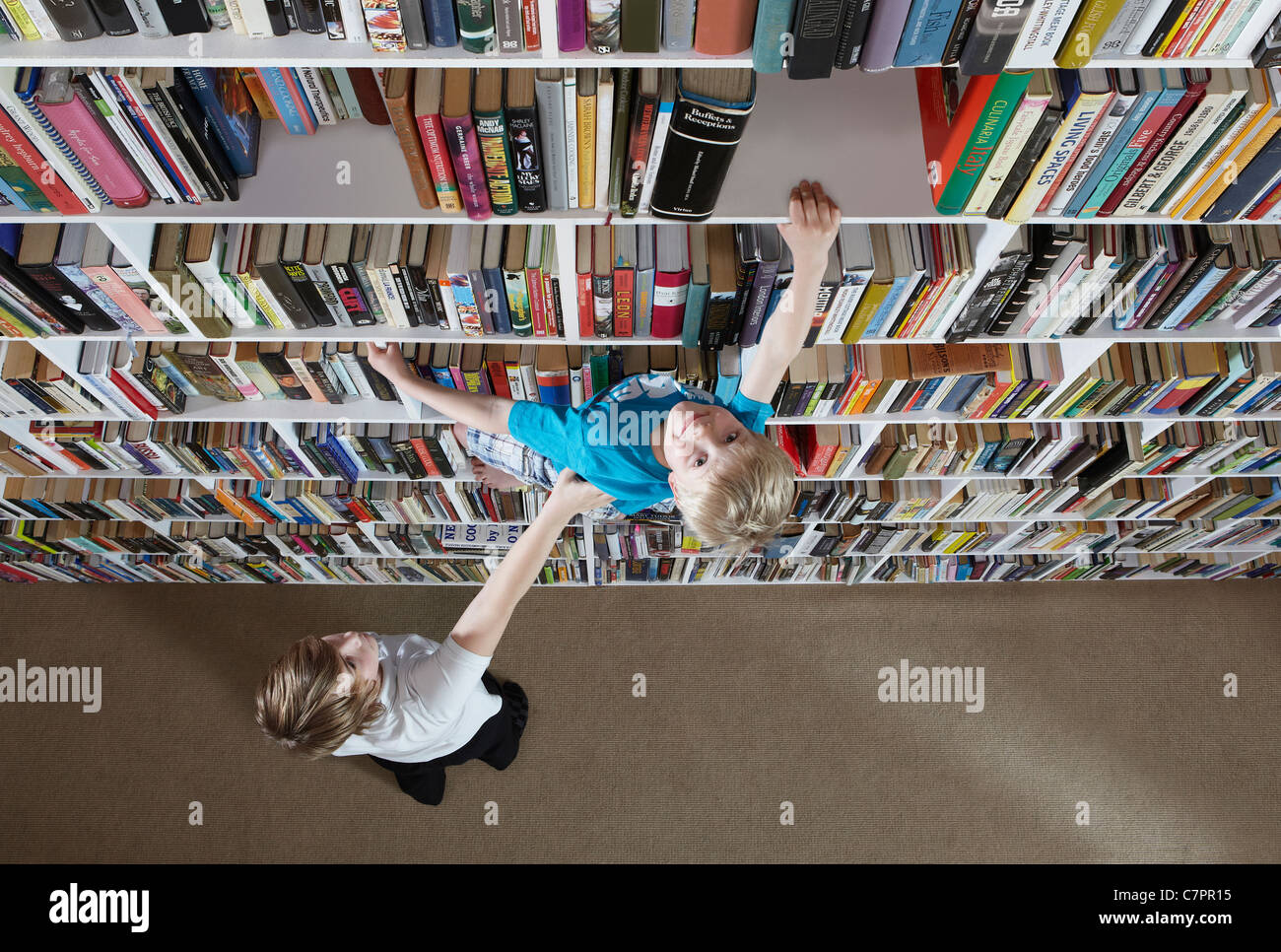 Girl helping boy climb bookshelves Stock Photo