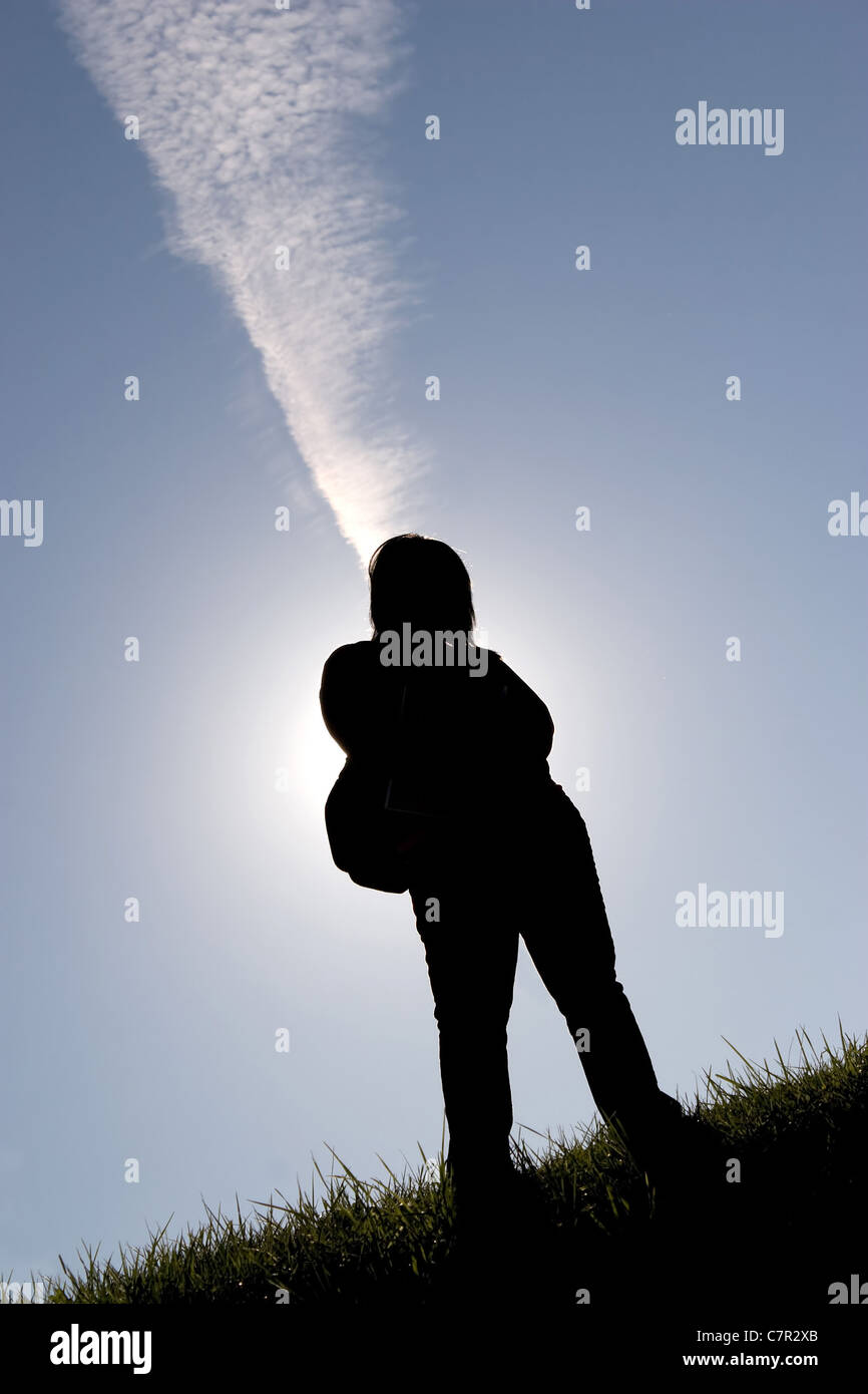 Silhouette of a student wearing a backpack back lit standing in a field outdoors. Stock Photo