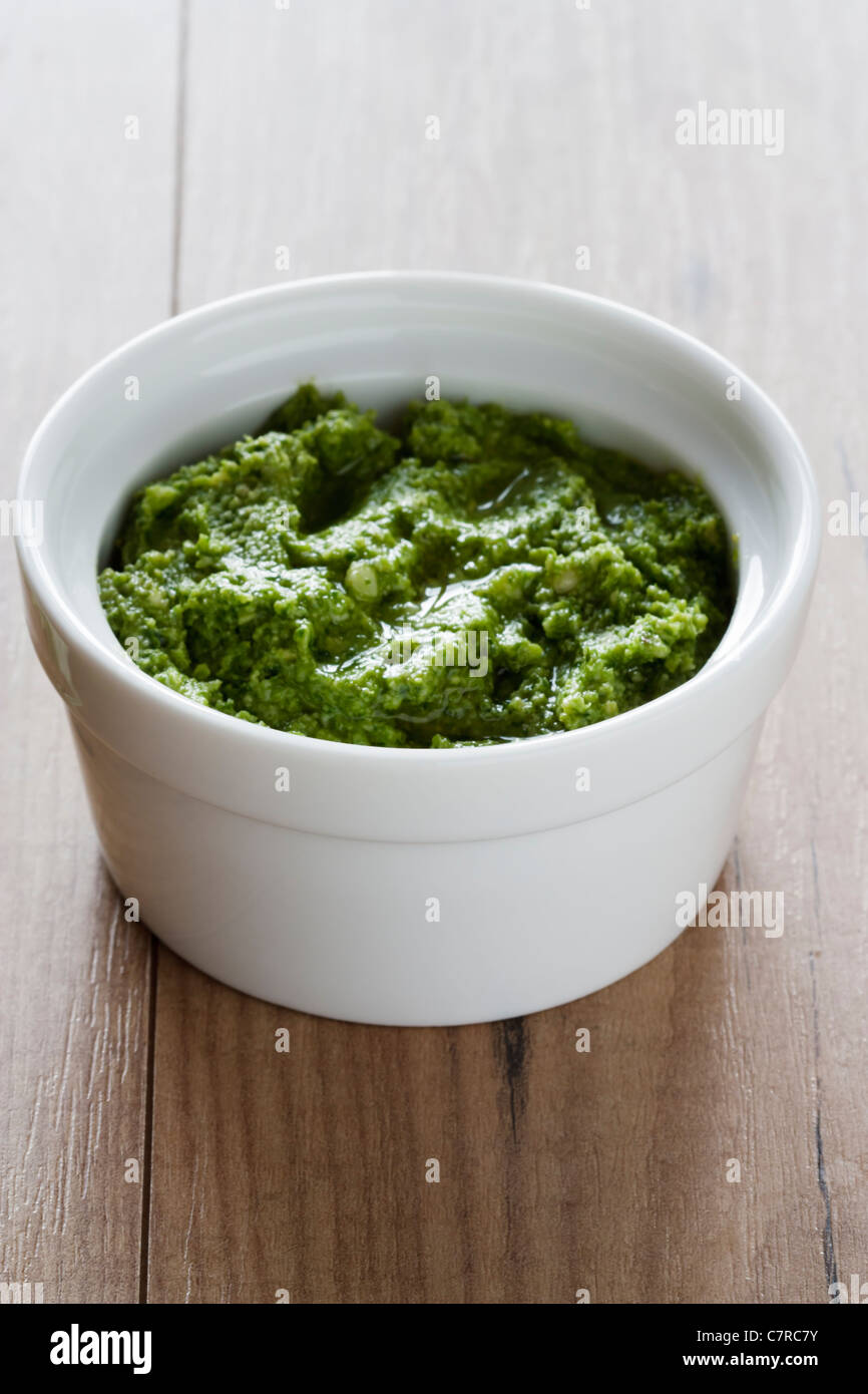 A small white bowl of fresh prepared rocket pesto with  copy space on a wooden background. Stock Photo