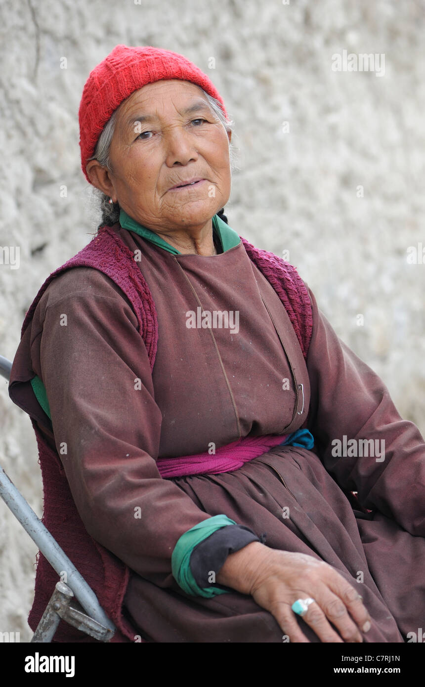 A woman sits by the road near a prayer wheel, chatting to passers-by.  Sumar, Nubra Valley, Ladakh, Republic of India. Stock Photo
