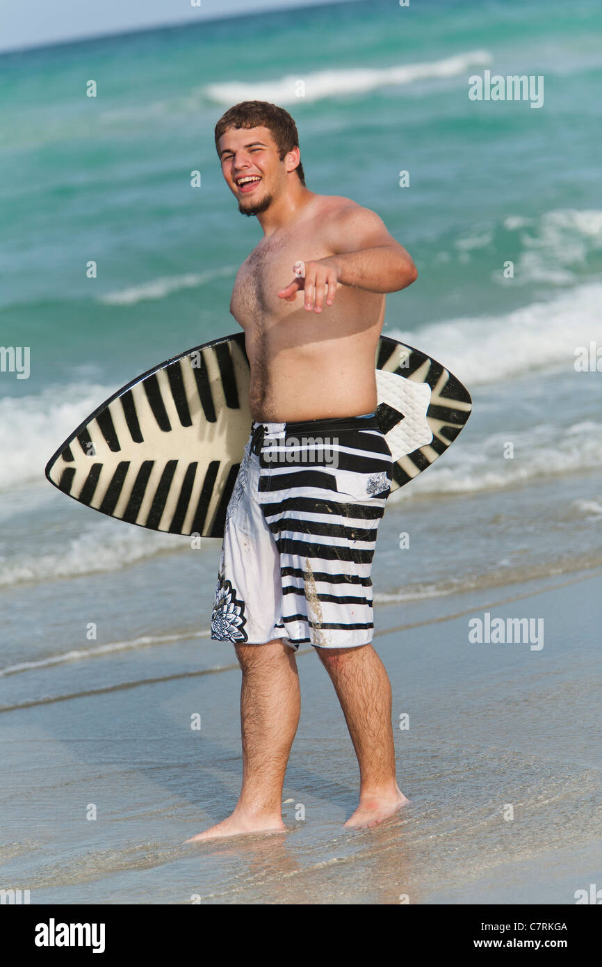 Teenage boy holding skimboard on the beach, smiling, portrait Stock