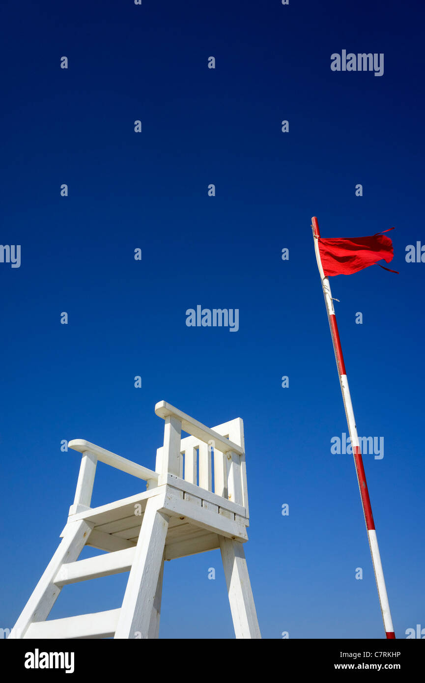 Red flag flying at a beach warning not to enter the water next to lifeguard's chair Stock Photo