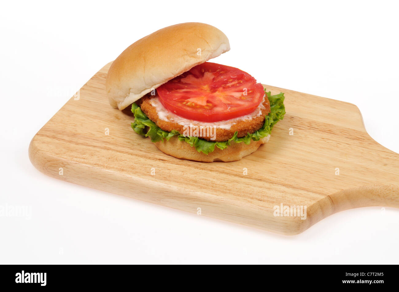 Open chicken burger patty sandwich with lettuce and tomato on a bread roll on a wood cutting board on white background cutout. Stock Photo