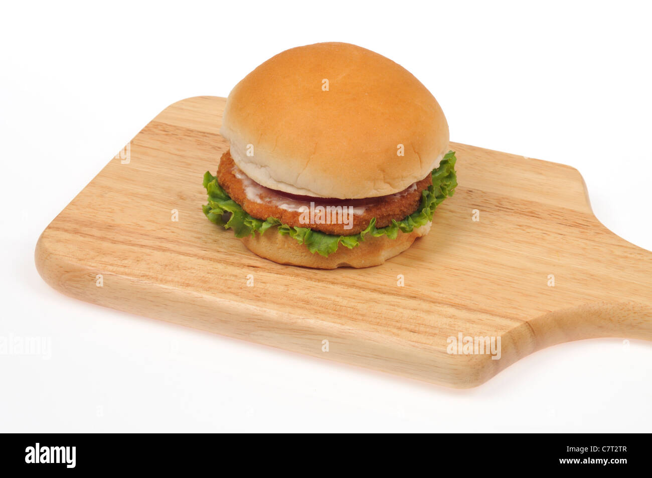 Chicken burger with lettuce and tomato on a bread roll on a wood cutting board on white background cutout. Stock Photo