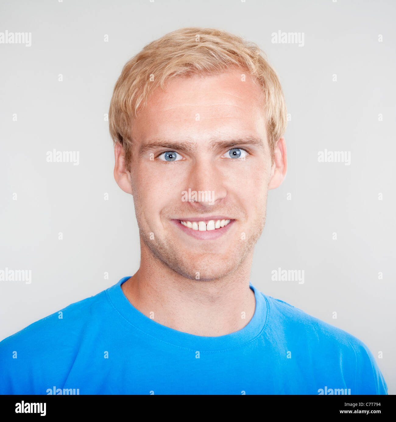 portrait of a young man with blond hair smiling - isolated on light ...