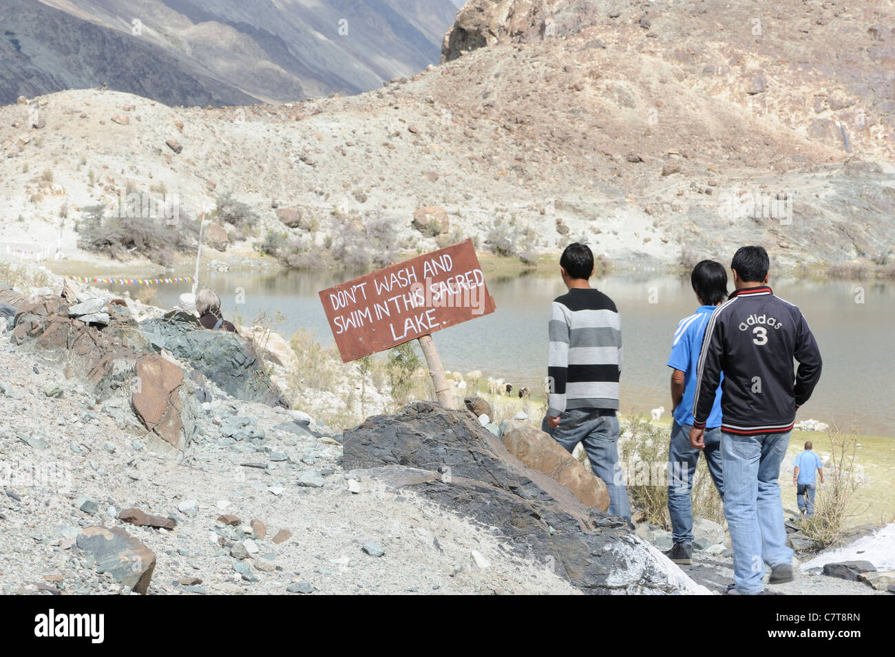 Young men approaching a sacred lake near Sumar. There is a sign saying 'Don't wash ans swim in this sacred lake'. Stock Photo
