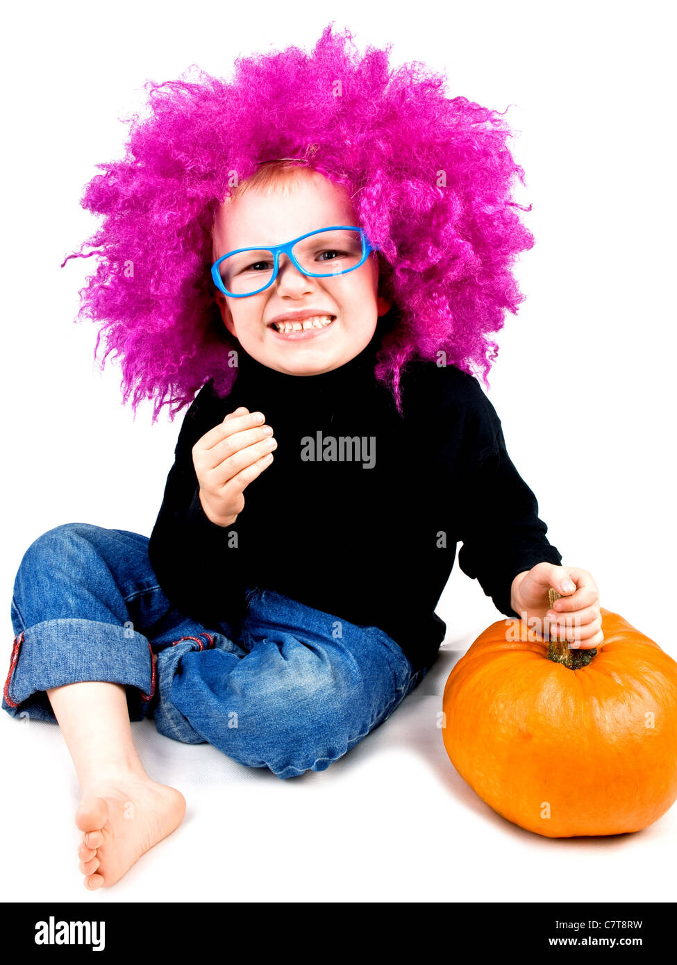 Cute little boy in big pink wig with Halloween pumpkin making funny
