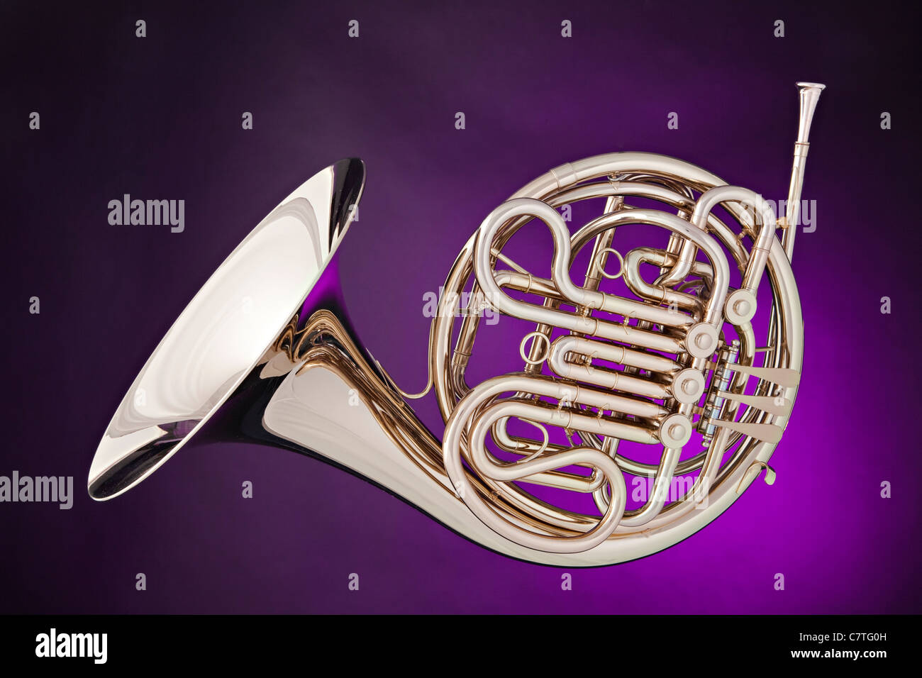 A silver French horn isolated against a spotlight purple background