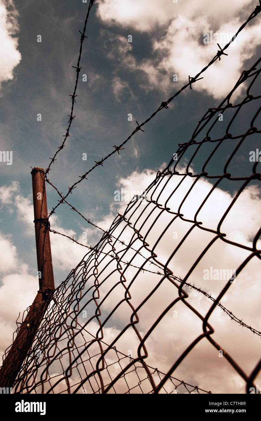 Barbed wire fence against a blue sky with clouds Stock Photo - Alamy