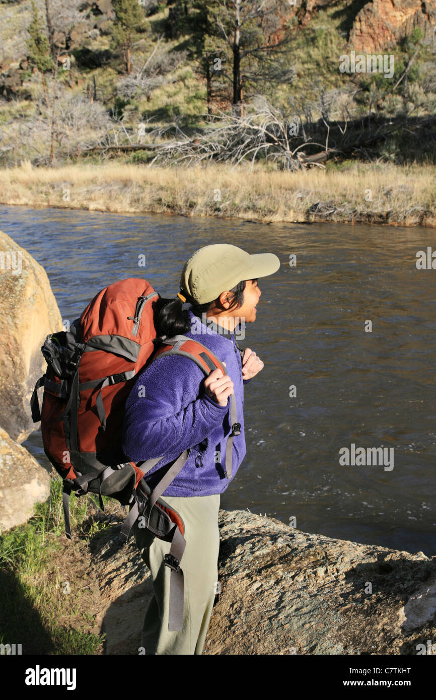 side view of a woman backpacker standing on a rock next to a river Stock Photo