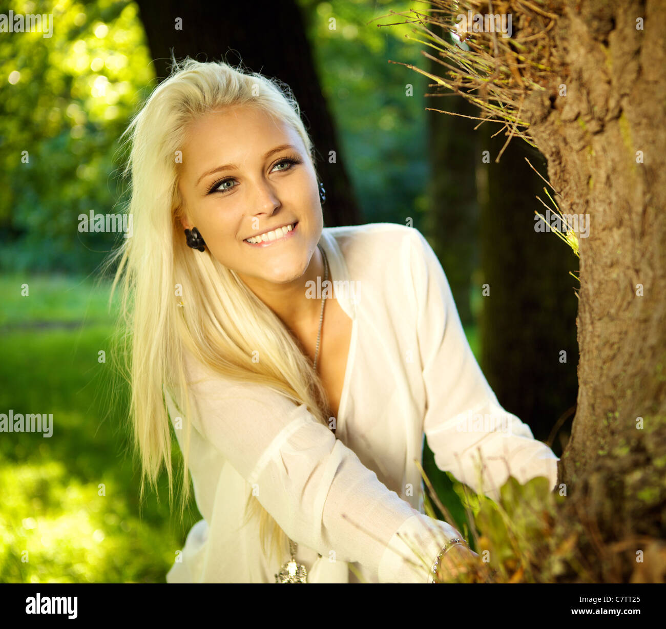 Pretty woman playing hide and seek in a park - looking out from behind a tree. Stock Photo