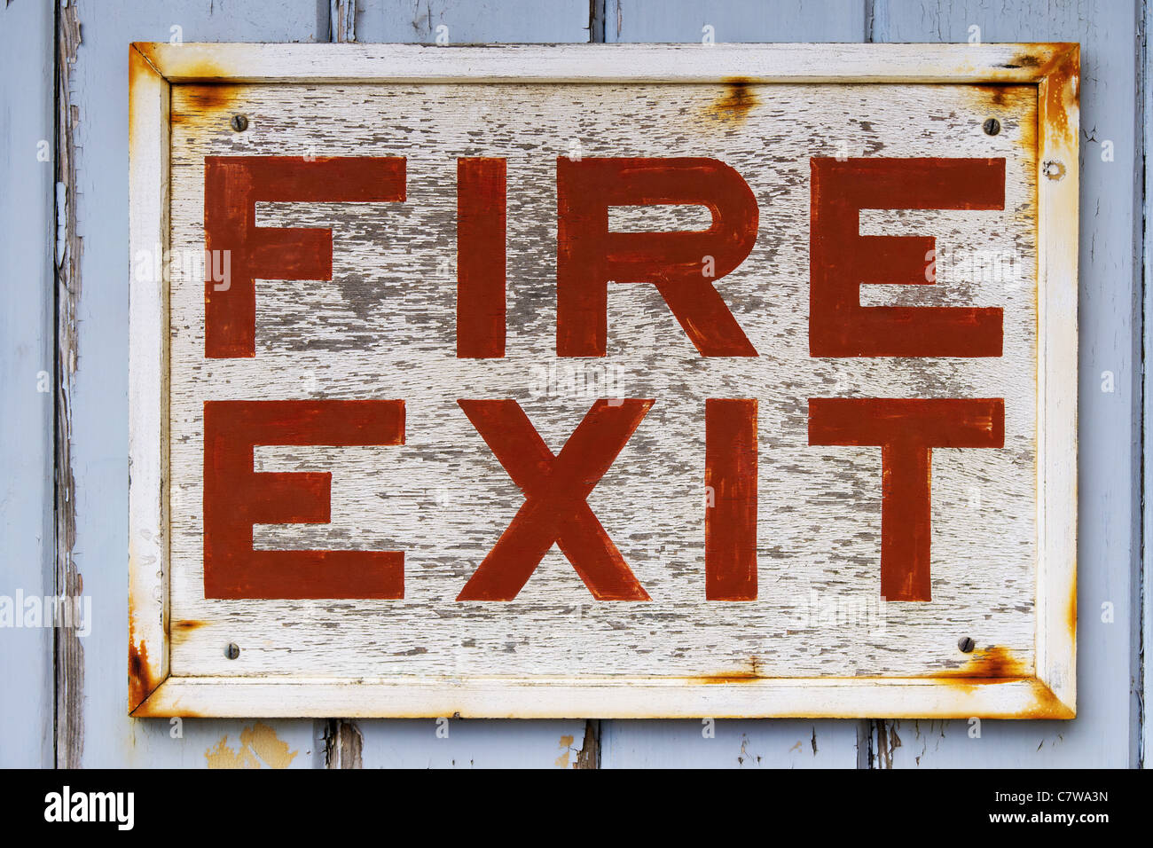 Photo of an old weathered FIRE EXIT sign on a blue door with peeling paint. Stock Photo