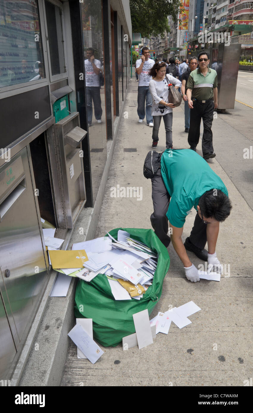 Mailman picking up envelopes fallen from his bag under a post box in Hong Kong Stock Photo