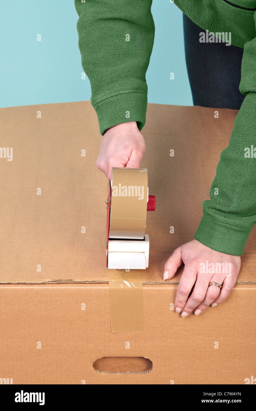 Photo of a womans hands taping up a cardboard box, can be used for removal or logistics related themes. Stock Photo