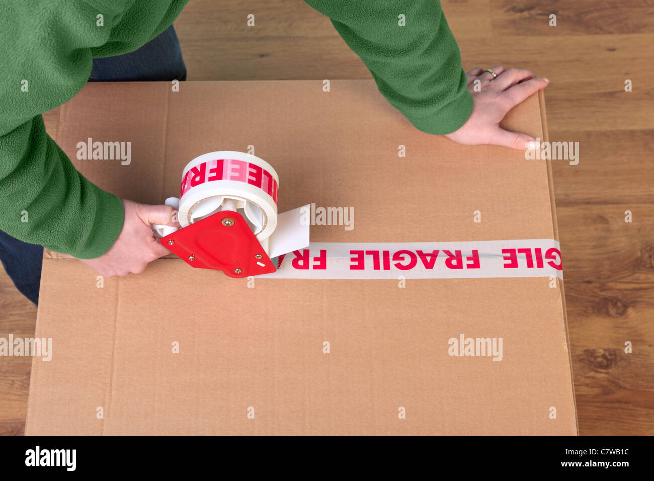 Photo of a womans hands taping up a cardboard box, can be used for removal or logistics related themes. Stock Photo