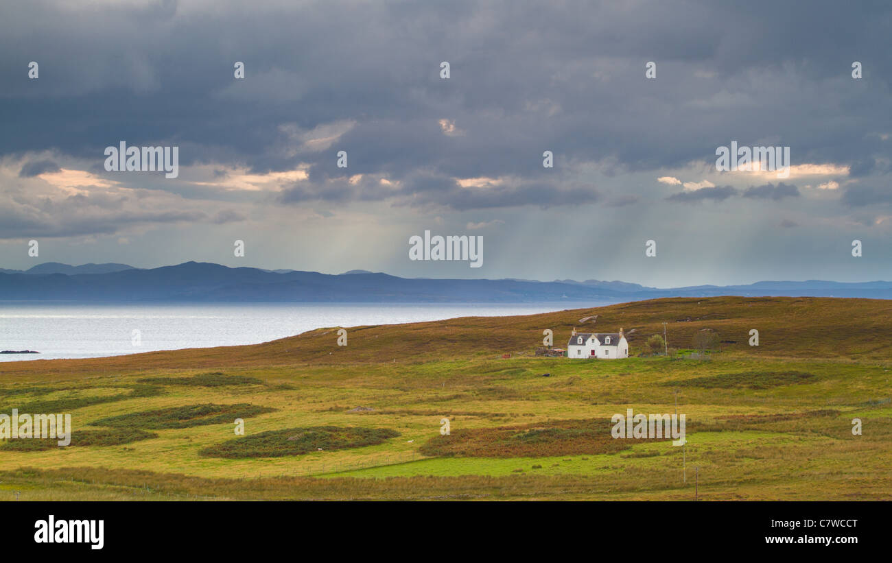 Small white abandoned house sitting on a Scottish hillside with a rain shower approaching over the distant mountains and loch. Stock Photo