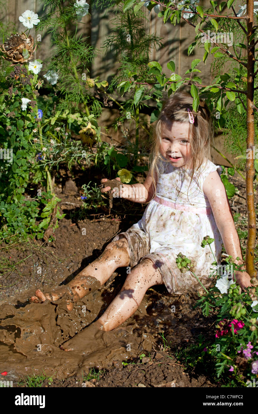 young girl sat in muddy puddle splashing around Stock Photo