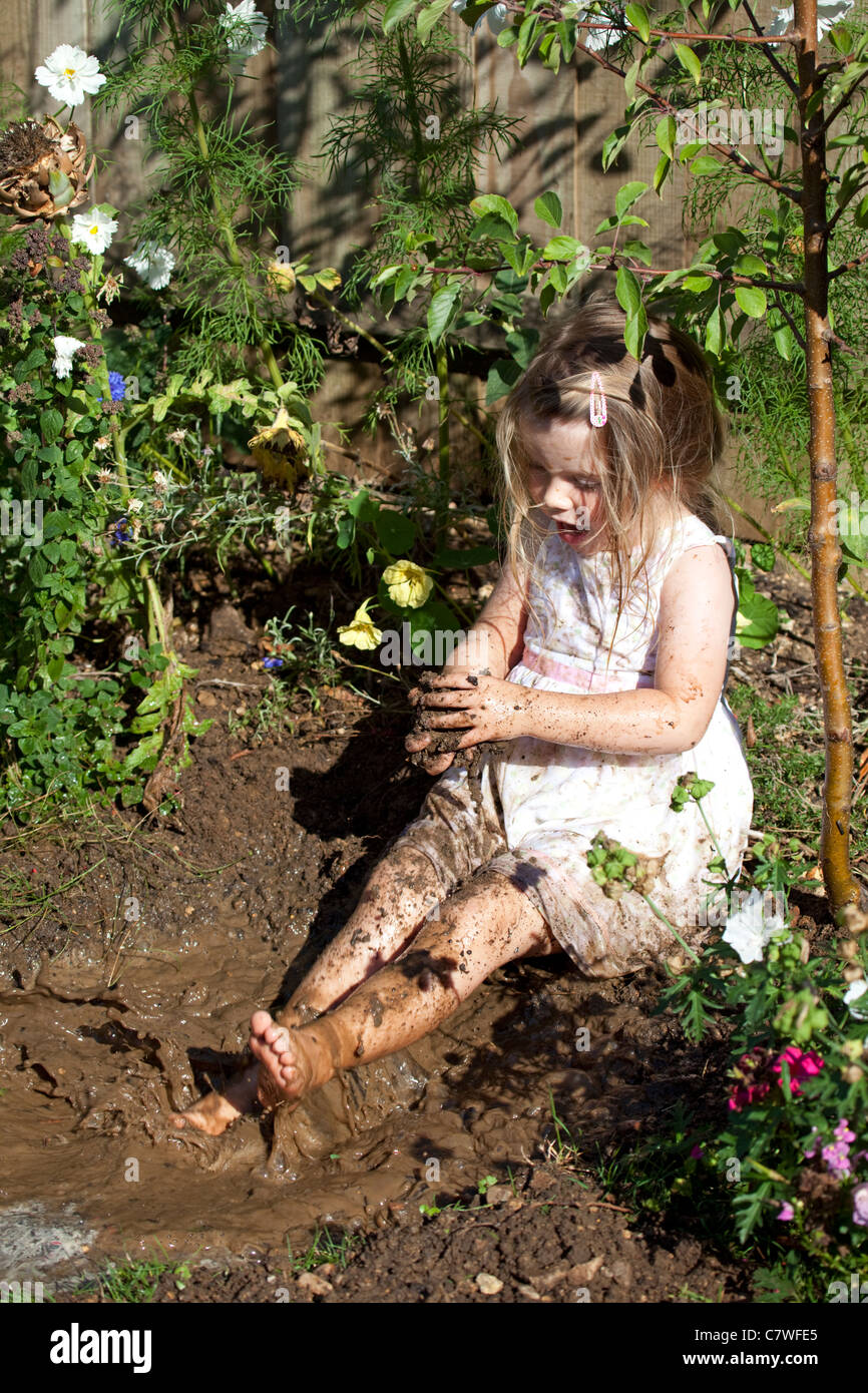 young girl wearing pretty dress sat in muddy puddle splashing around Stock Photo