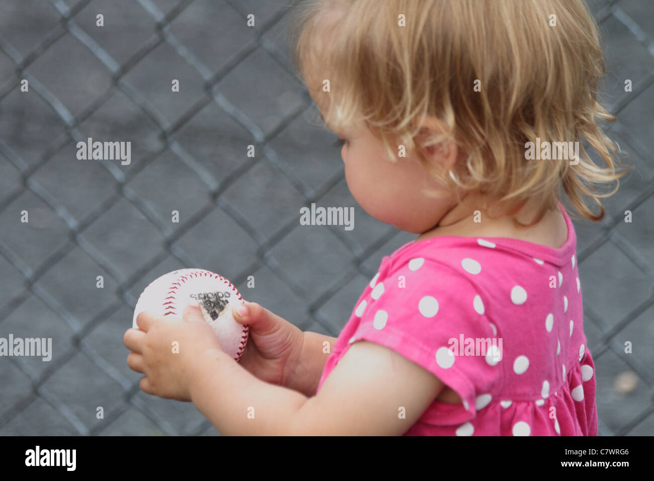 toddler girl with baseball looking and wondering what to do with ball Stock Photo