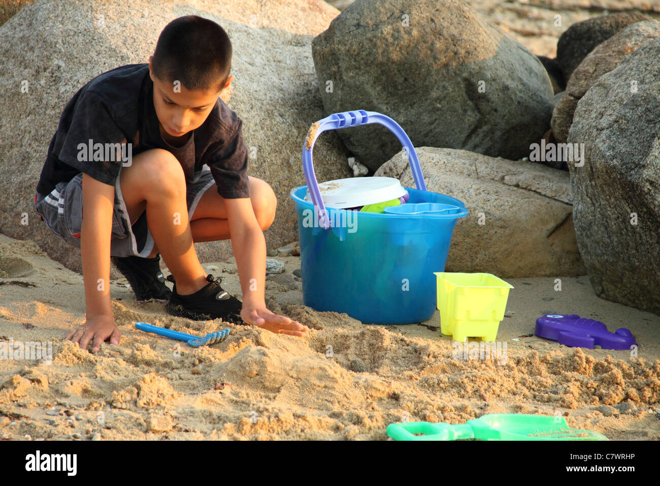 boy digging in sand sunset shining sand toys buckets rake shovel